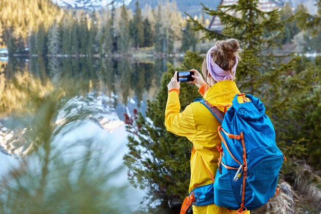 O viajante da liberdade tira fotos da vista panorâmica da natureza, tenta capturar o belo lago com montanhas e floresta, fica para trás