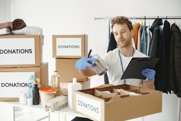 O voluntário coleta coisas de doações. O cara embala caixas com coisas. O homem compara a dotação.