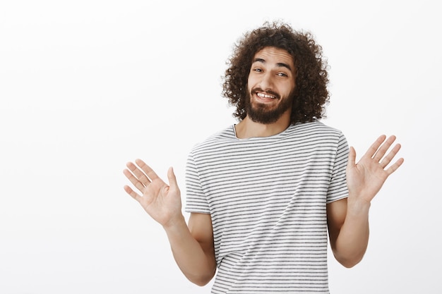 Obrigado, mas eu passo. Despreocupado e bonito cara oriental com cabelo encaracolado, levantando as palmas das mãos e acenando perto do peito em um gesto de rejeição, sorrindo sem jeito e negando envolvimento