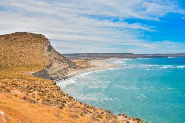 Oceano lindo e calmo cercado por falésias sob o céu azul nublado