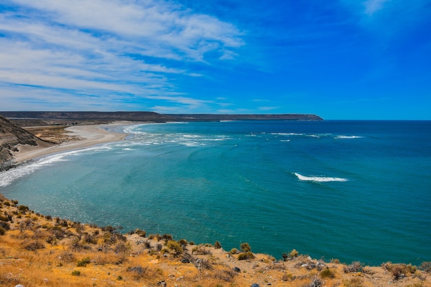 Oceano lindo e calmo cercado por falésias sob o céu azul nublado