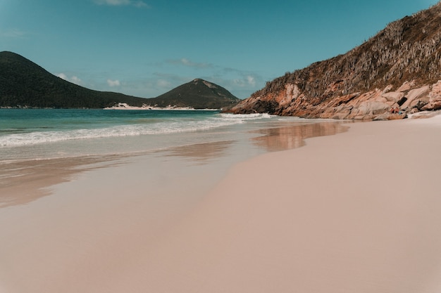 Oceano ondulado batendo na praia de areia cercada por montanhas no rio de janeiro