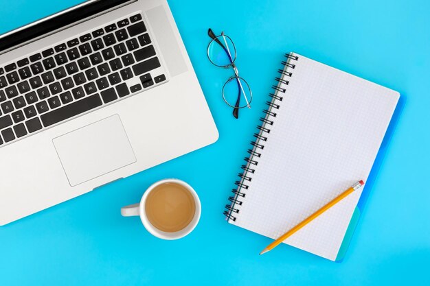 Óculos de laptop e xícara de café em um fundo azul