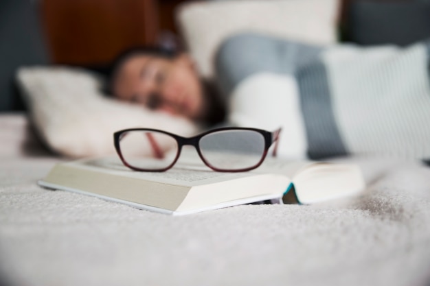 Óculos e livro perto da mulher adormecida