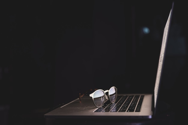 Foto grátis Óculos perto do laptop refletem a luz da tela no espaço escuro da cópia