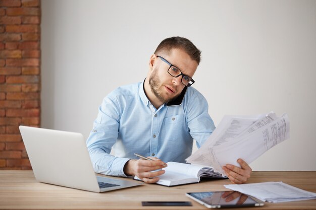 Ocupado empresário concentrado de óculos e camisa, sentado em um escritório confortável
