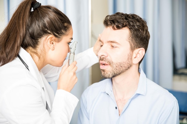 Oftalmologista feminina usando um otoscópio para examinar os olhos de um paciente em sua clínica