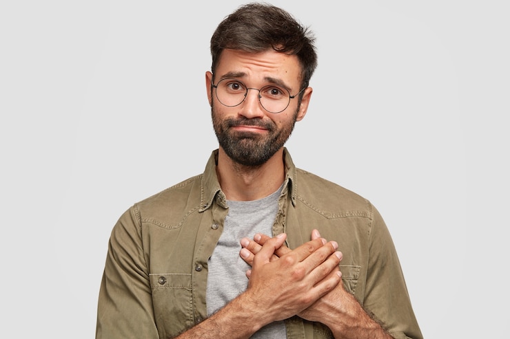 Foto grátis oh, muito obrigado! jovem homem barbado atraente mantém as mãos no coração, expressa gratidão e fica de pé contra a parede branca. cara barbudo caucasiano agradecendo ao melhor amigo