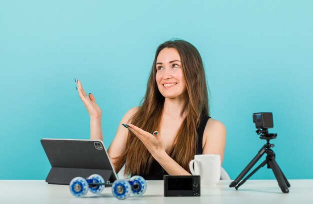 Olhando para cima a garota do blogueiro está posando apontando para cima com as mãos no fundo azul