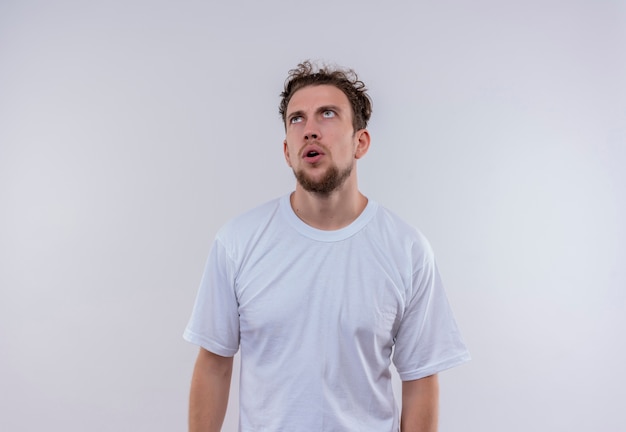 Olhando para cima pensando em um cara jovem vestindo uma camiseta branca em um fundo branco isolado