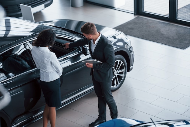 Olhando para o interior do veículo. Cliente do sexo feminino e empresário barbudo elegante e moderno no salão automóvel