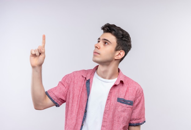 Olhando para o lado de um jovem caucasiano com uma camisa rosa apontando para cima na parede branca isolada