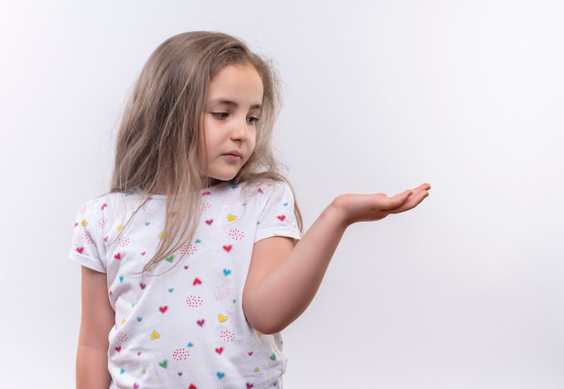 Foto grátis olhando para o lado, menina triste da escola vestindo camiseta branca levantando a mão na parede branca isolada