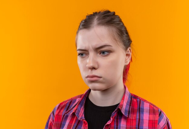 Olhando para o lado pensando em uma jovem mulher bonita vestindo uma camisa vermelha na parede amarela isolada