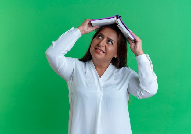 Olhando para uma mulher caucasiana de meia-idade satisfeita e casual coberta com um livro na cabeça