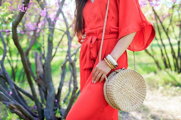 Olhar na moda de primavera, mulher segurando um saco de palha de rattan boêmio da moda elegante de Bali e usando vestido boho coral.