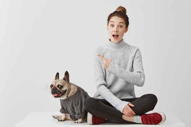 Olhe ali! Surpresa mulher apontando o dedo indicador pedindo atenção em algo digno. Modelo feminino gesticulando significa que isso é legal na companhia do cão. Conceito de estilo de vida, cópia espaço