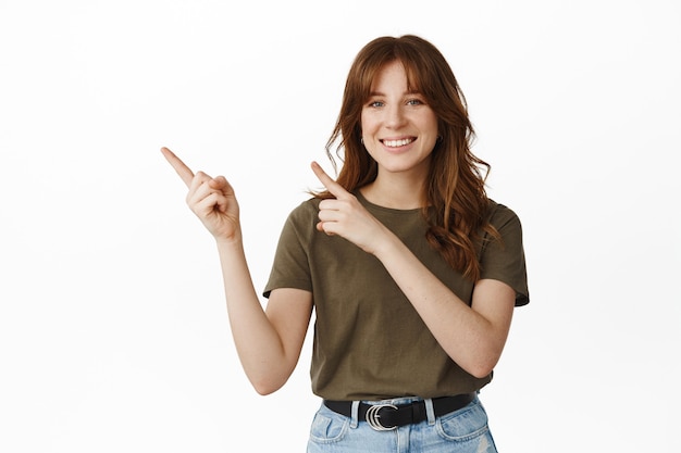 Olhe assim. Mulher jovem sorridente e feliz apresenta o logotipo da empresa, apontando o dedo para o canto superior esquerdo e parecendo amigável, de pé no branco