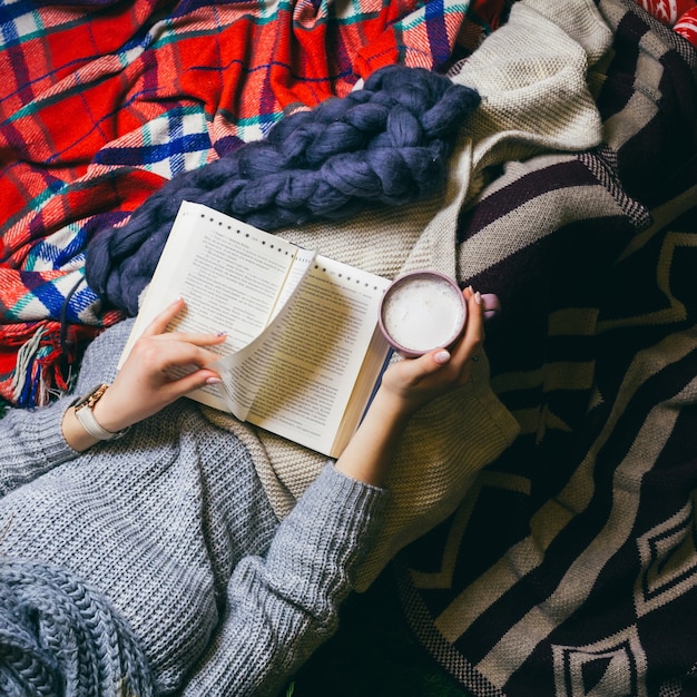 Olhe de cima na jovem senhora bebendo café enquanto ela lê um livro