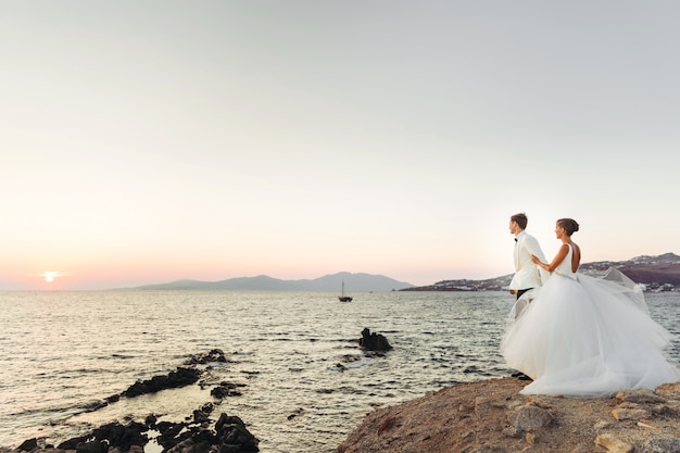 Olhe de longe no lindo casal de noivos assistindo o pôr do sol sobre o mar