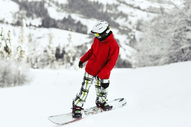 Olhe por trás do snowboarder em jaqueta vermelha em montes cobertos de neve