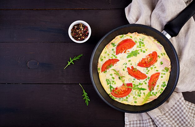 Omelete com tomate, presunto e cebola verde na mesa escura