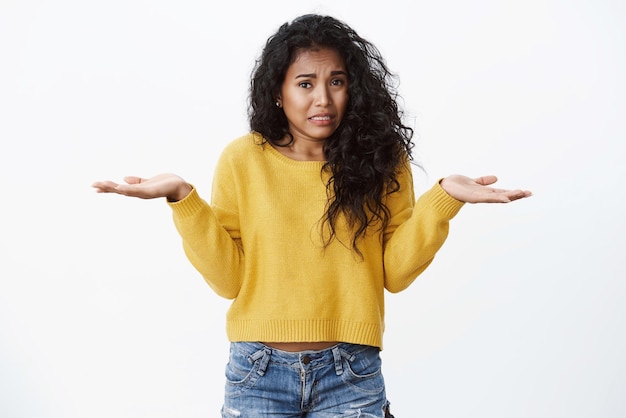 Foto grátis opa garota pede desculpas mulher afro-americana boba bonita cabelo preto encaracolado encolhendo as mãos espalhadas de lado franzindo a testa e chorando como se sentindo preocupado se desculpando se desculpando cometendo um erro ficar de fundo branco