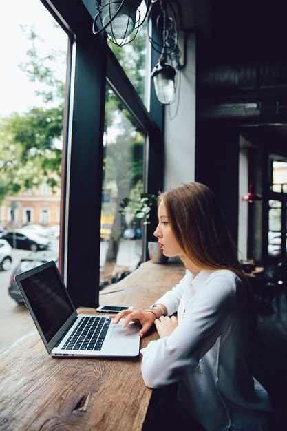 Opinião lateral a mulher de negócios pensativa encantador que usa um portátil, ao sentar-se no café.