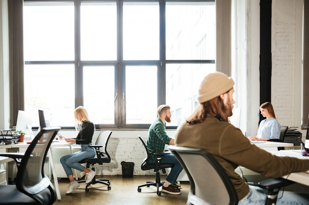 Os colegas trabalham no escritório usando computadores. Olhando de lado.