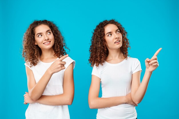 Os gêmeos de duas mulheres sorrindo, apontando os dedos para longe sobre o azul.