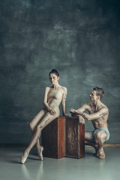 Os jovens bailarinos modernos com tatuagens no corpo posando no fundo cinza do estúdio
