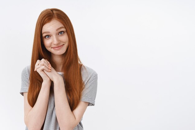 Os olhos azuis da menina ruiva jovem e carismática fofa tocaram um gesto agradável e comovente, apertar as mãos agradecido, sorrindo, encantado, agradecendo, namorado, lindo presente romântico, parede branca