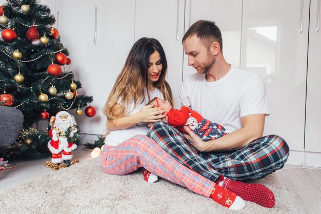 Os pais lindos abraçando a filha e sentado perto da árvore de Natal