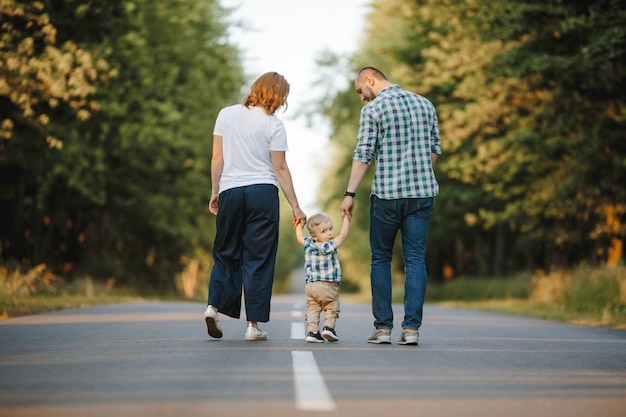 Os pais segurando seu filho pequeno estão andando por uma estrada