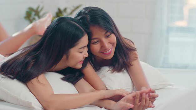 Os pares asiáticos das mulheres do lgbtq da lésbica beijam e abraçam na cama em casa.