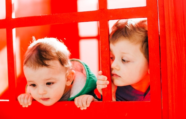 Os pequenos meninos estão perto da parede vermelha