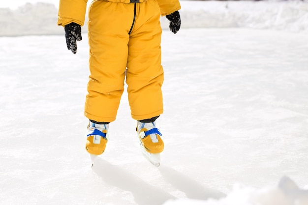 Os pés de uma criança em pé em uma pista de gelo em sapatos patins ensinando crianças a patinar