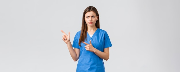 Os profissionais de saúde evitam o seguro de vírus e o conceito de medicina algo errado enfermeira ou médico desagradado sério em jaleco azul franzindo a testa olhando e apontando para a esquerda preocupada