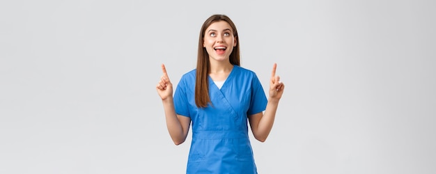 Foto grátis os profissionais de saúde previnem o conceito de medicina de triagem de teste de vírus covid19 alegre e sorridente médica ou enfermeira em uniforme azul apontando os dedos para cima e olhando para cima regozijando-se