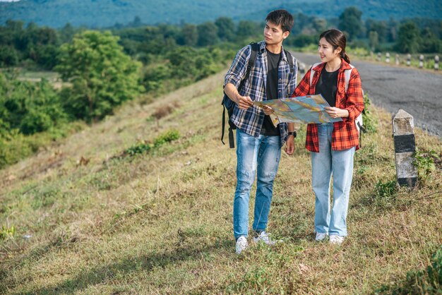 Os turistas masculinos e fêmeas em pé olham para o mapa na estrada.