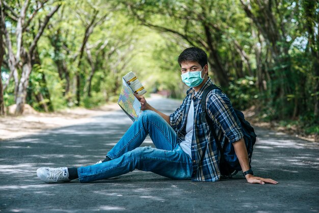 Os turistas masculinos sentam e olham para o mapa na estrada.