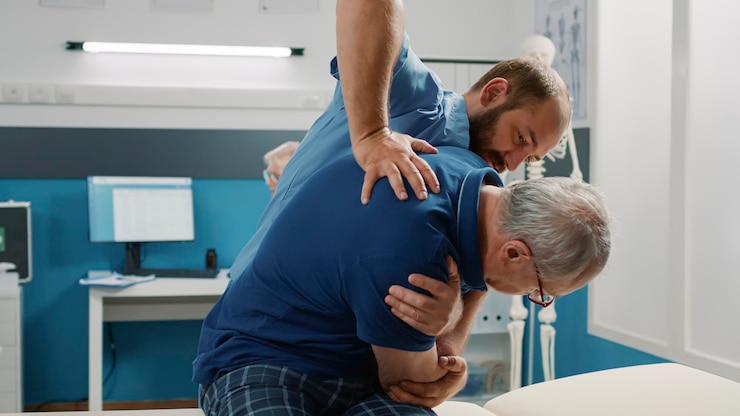 Foto grátis osteopata ajudando o homem sênior a quebrar os ossos das costas no gabinete, fazendo exercícios de fisioterapia. assistente masculino usando procedimento de fisioterapia para aumentar a mobilidade e tratar o paciente.