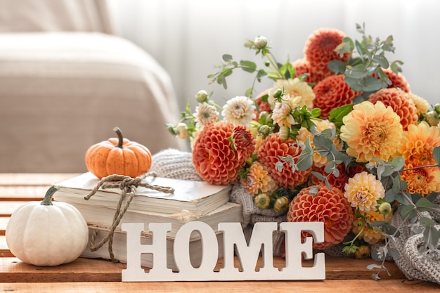 Outono natureza morta com um buquê de flores de crisântemo, a palavra decorativa casa e abóboras em um fundo desfocado.