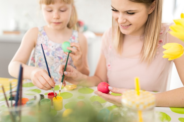 Outra e filha pintando ovos com escovas