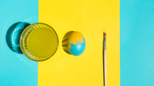 Ovo de Páscoa colorido com pincel e copo de água na mesa brilhante