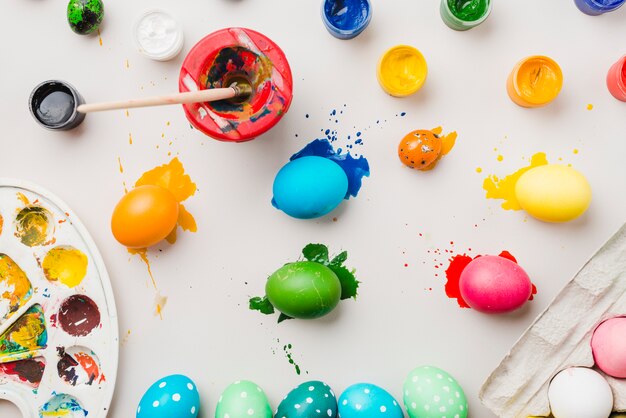 Ovos coloridos brilhantes perto de recipiente, pincel em lata, cores de água e paleta