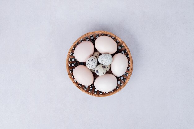 Ovos de codorna e ovos de galinha em uma tigela na superfície branca.