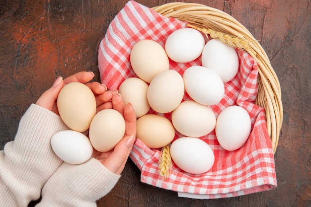 Ovos de galinha branca de vista superior dentro de uma cesta com uma toalha na mesa escura comida crua fazenda café da manhã foto colorida refeição