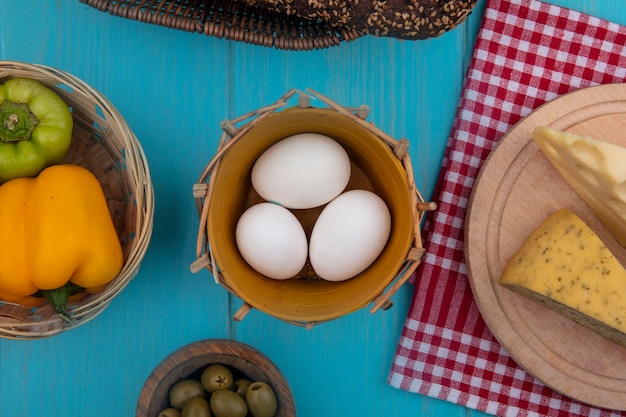 Foto grátis ovos de galinha com azeitonas, pimentões, iogurte de tomate em uma jarra e queijos em fundo turquesa