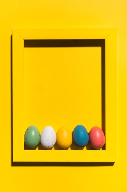 Foto grátis ovos de páscoa coloridos no quadro na mesa amarela